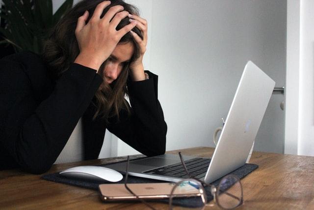 shocked woman holding her head in front of laptop