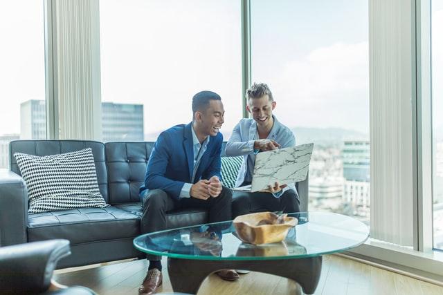 two man in suit in a high-rise apartment holding laptop in hand