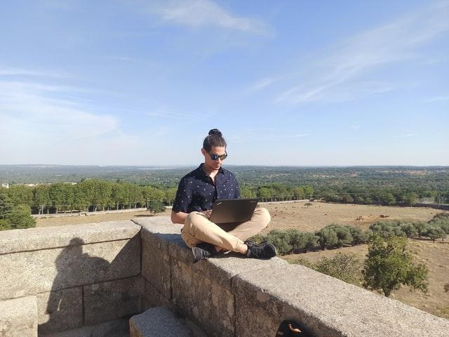 man sitting on top of a castle wearing sunglasses while working on laptop