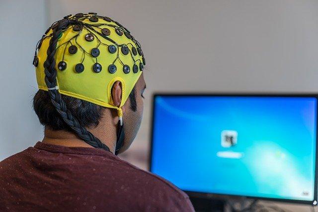 man wearing an Electroencephalogram or EEG cap in front of a monitor