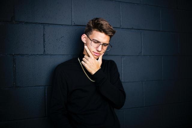 man wearing black leaning on wall while thinking