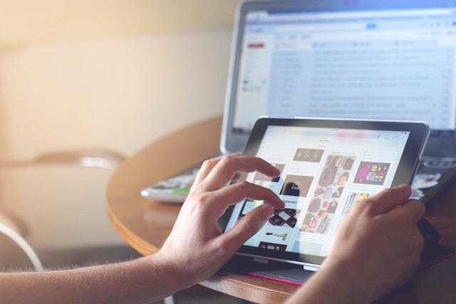 a person using iPad with MacBook in background