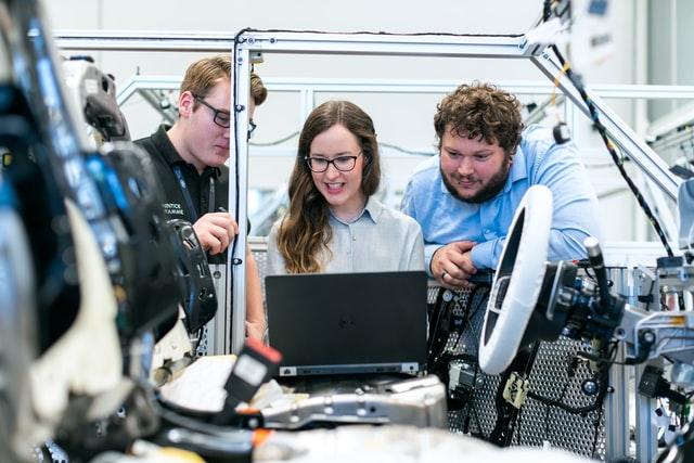 group of engineer looking at laptop in front of a car prototype