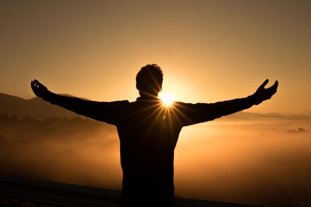 man silhouette infront of sunset while standing on a mountain 