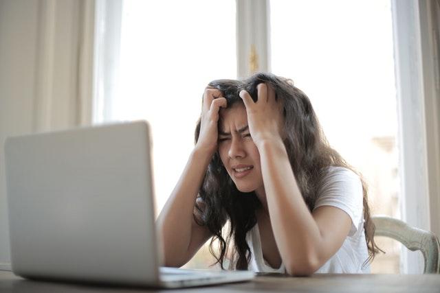 woman in white shirt showing frustration in front of a laptop