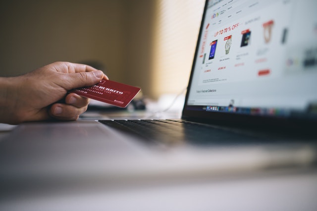 person holding credit card in hand in front a laptop for shopping online